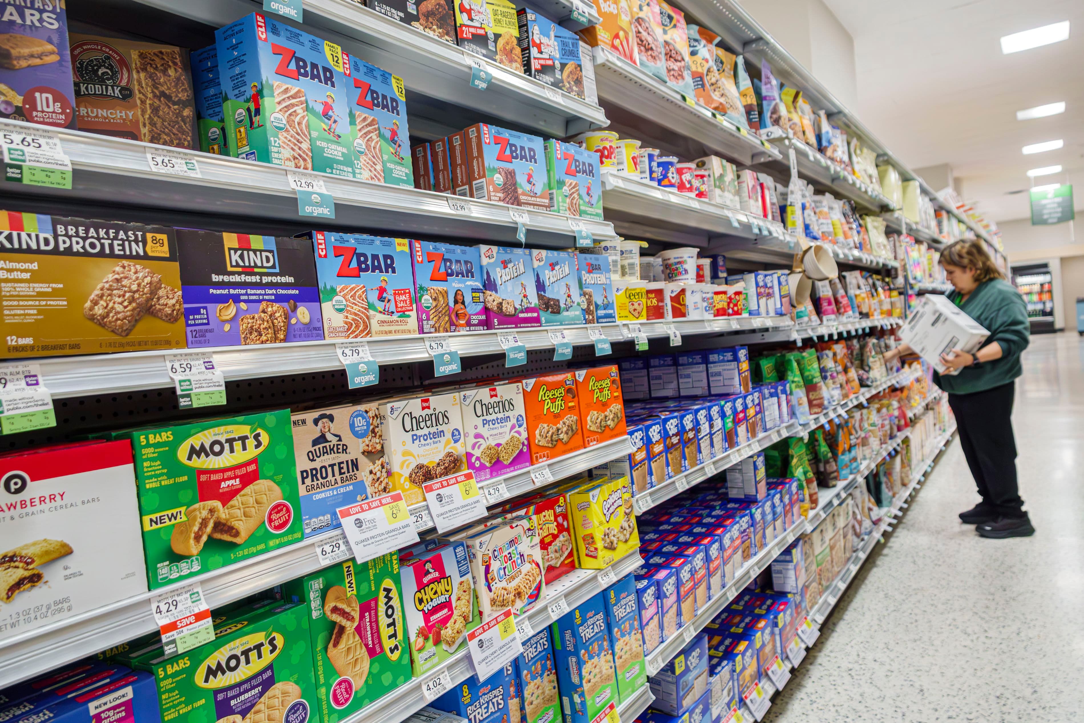 A woman looking at brands in a grocery store aisle
