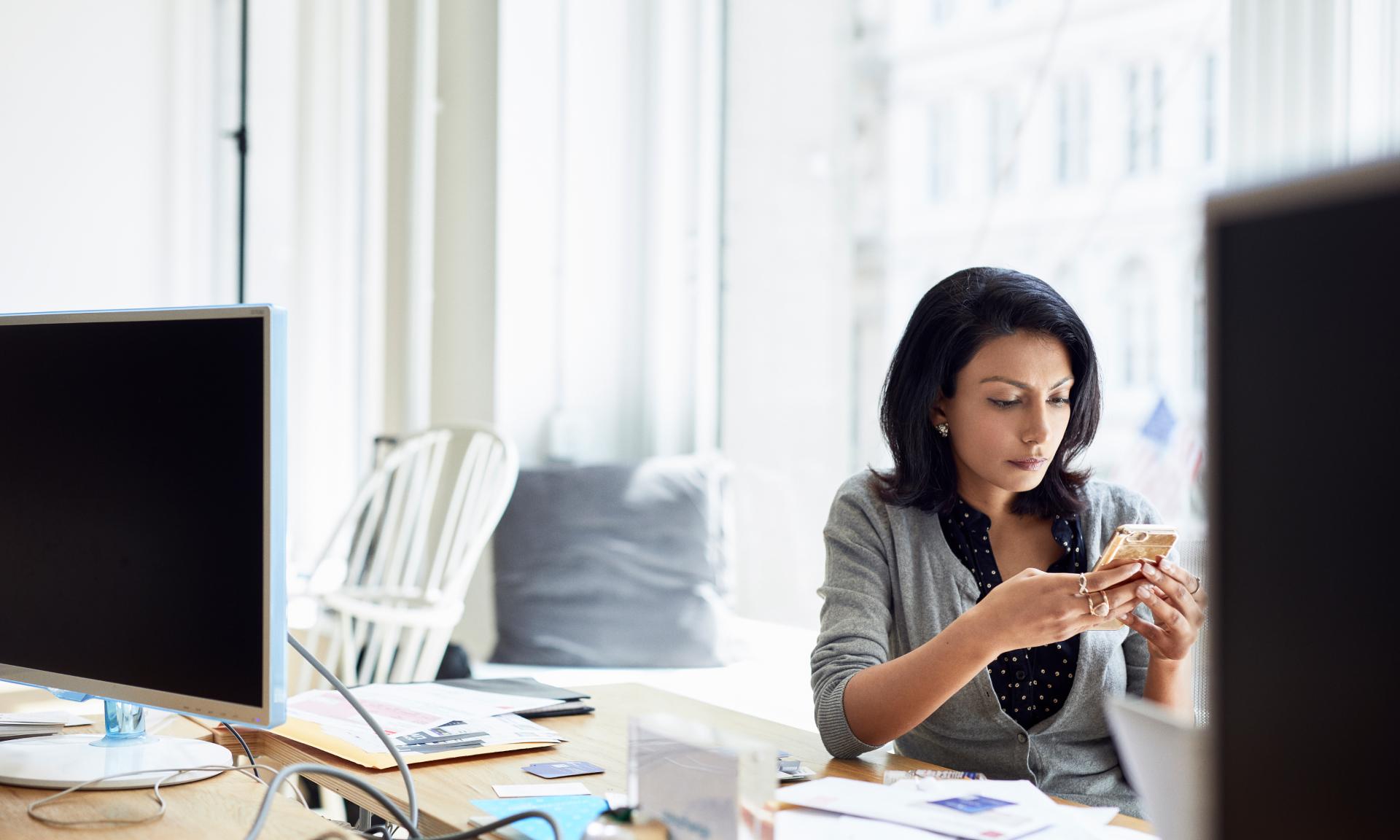 A woman on her phone at her desk.