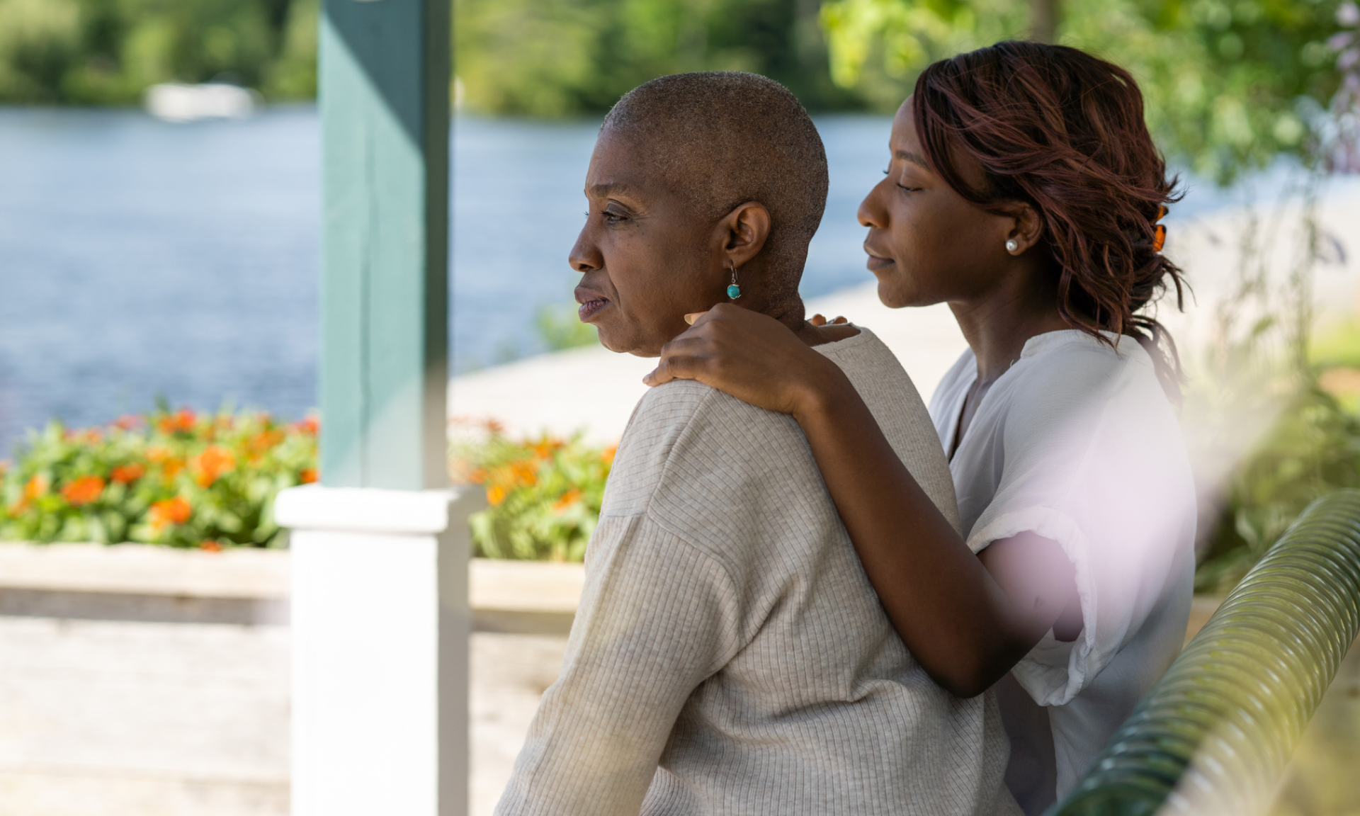 A young Black woman and an older Black woman sit on a bench in a park together