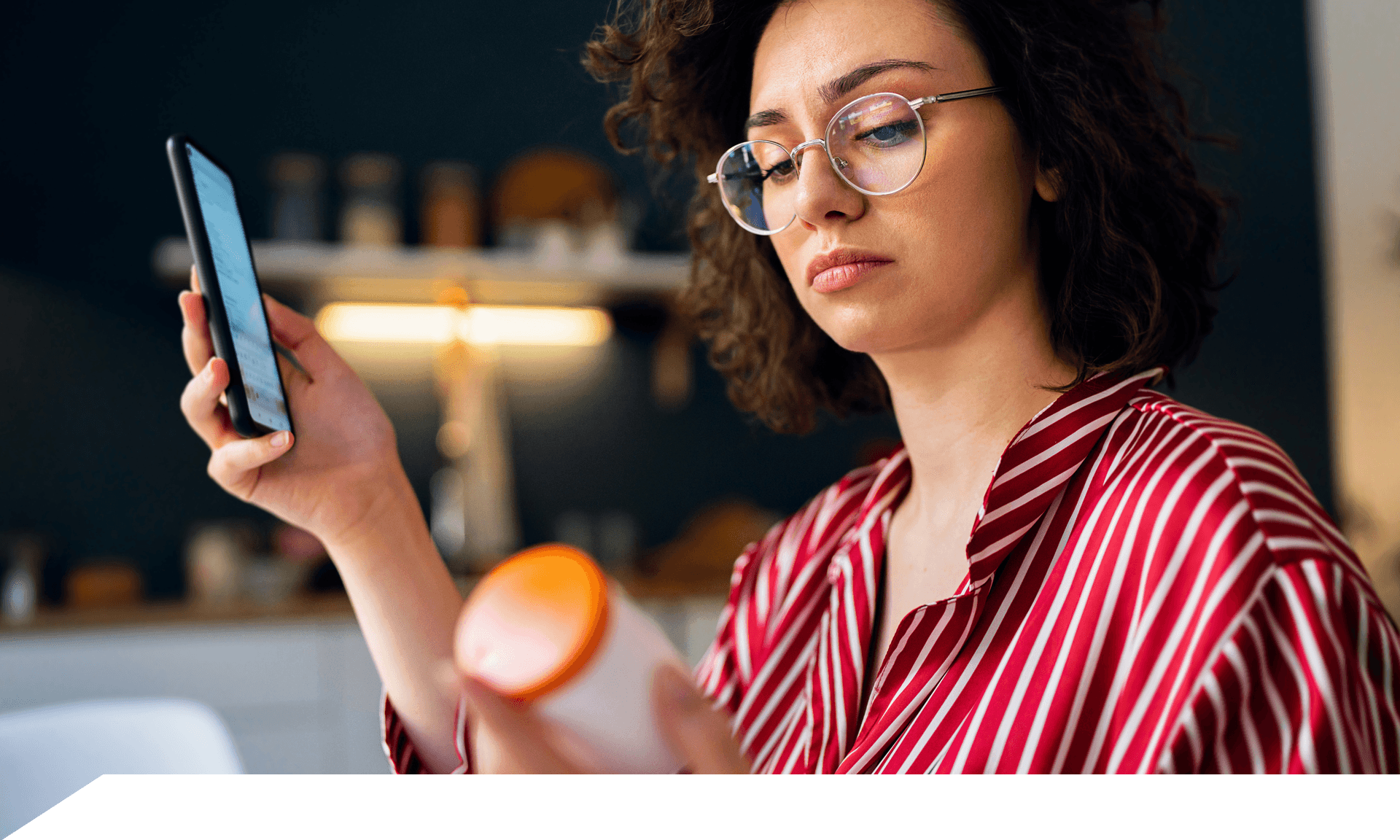 A woman looking at a pill bottle and holding her phone