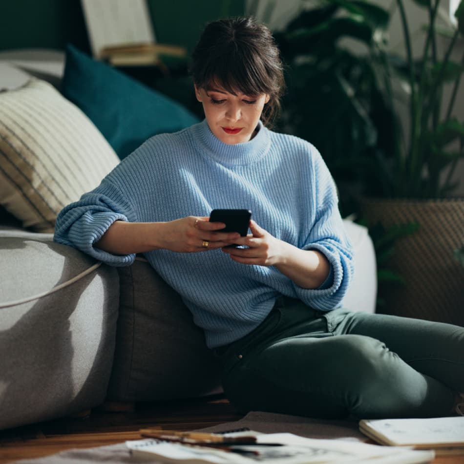 woman sitting next to couch on her phone