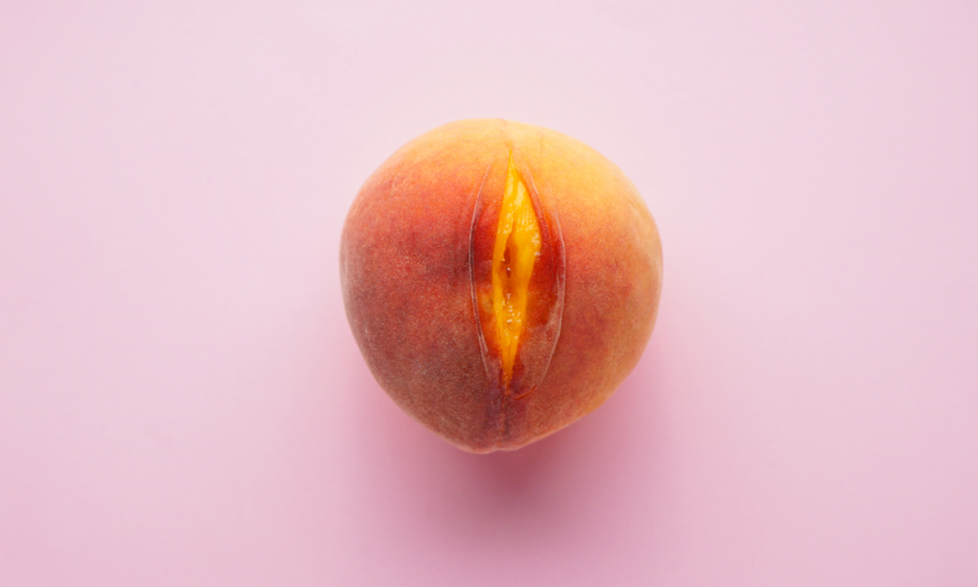 A peach slightly cut to look like a vulva on a pink background