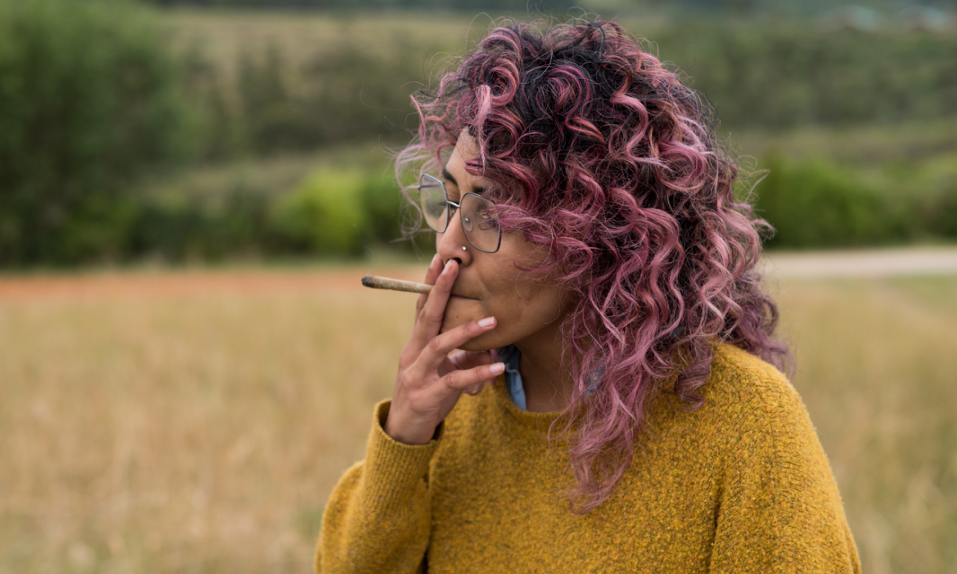 A woman with pink curly hair smoking a joint outside