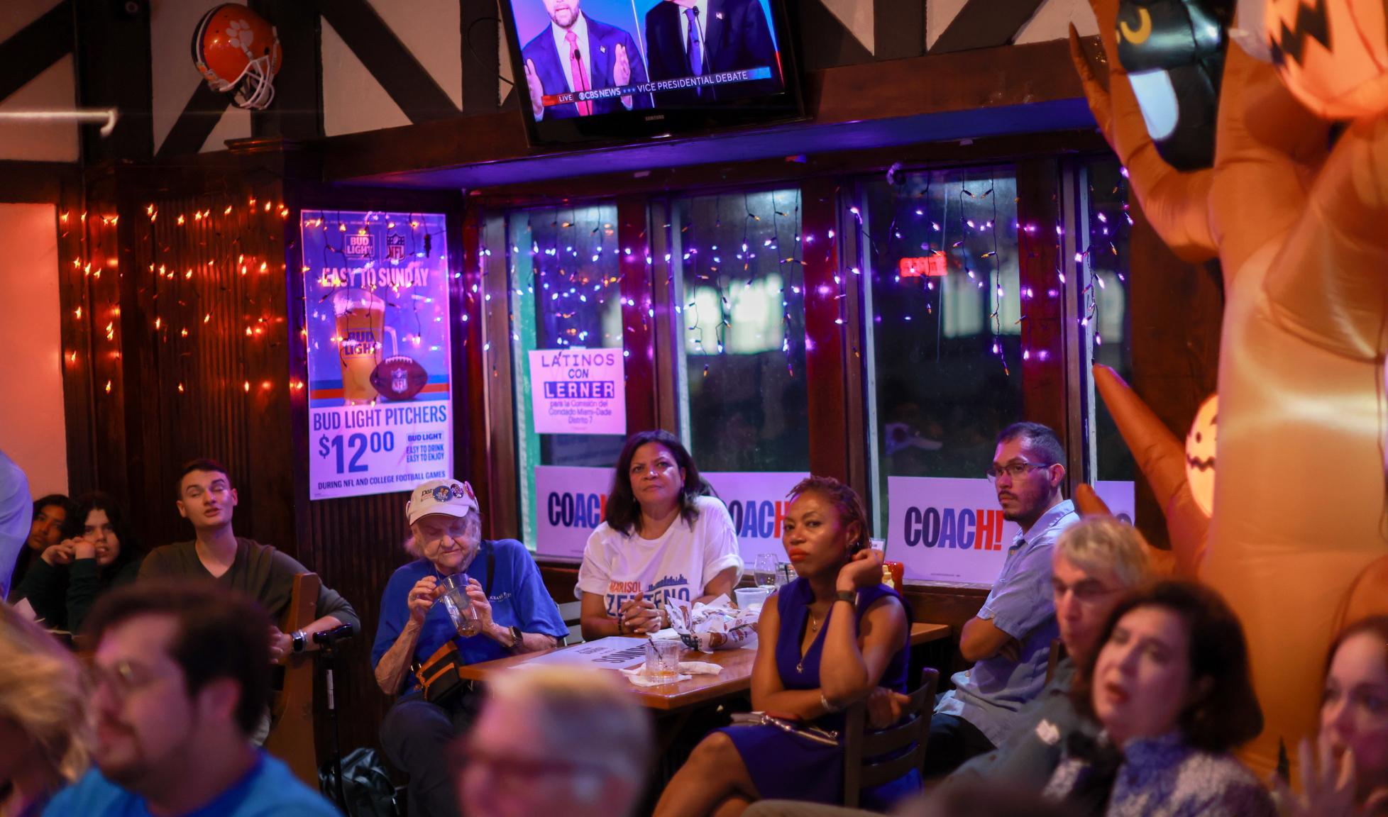 People watch as Republican vice presidential candidate U.S. Sen. J.D. Vance (R-OH) and Democratic vice presidential nominee Minnesota Gov. Tim Walz appear together during the CBS News Vice Presidential Debate on October 01, 2024 in Kendall, Florida.