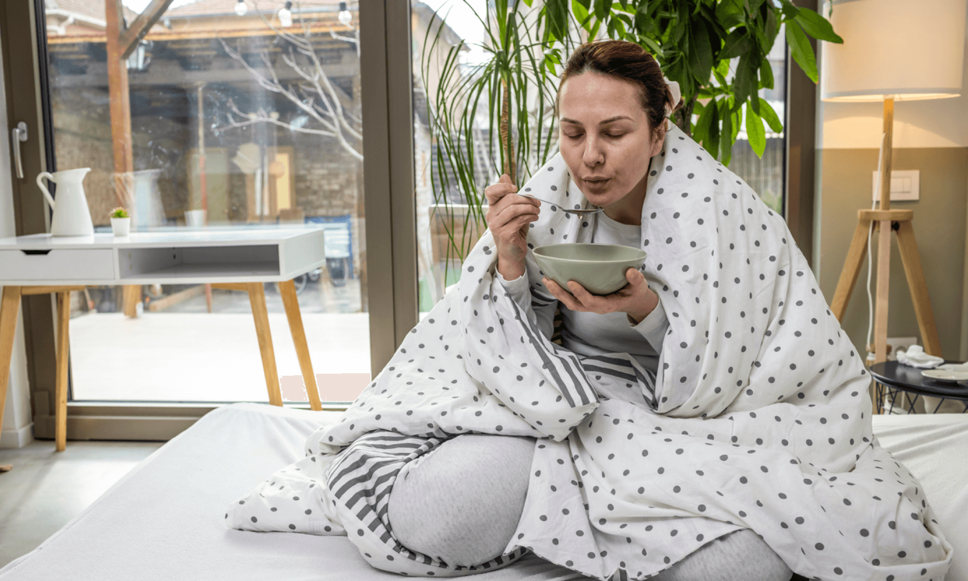 A woman wrapped in a blanket eating soup